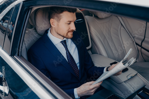 Thoughtful executive manager in formal suit reading newspaper in backseat of limousine photo