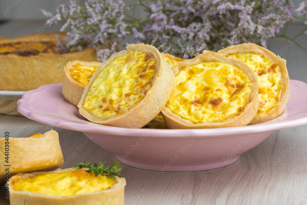 cheese lorraine quiches on a pink plate, some cheese and mint decorative elements, wooden base cheese lorraine quiches on a pink plate, some cheese and mint decorative elements, wooden base