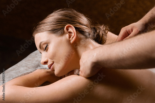 Attractive girl is relaxing on classic massage procedure in spa. Manual therapy. Masseur is doing shoulder massage.