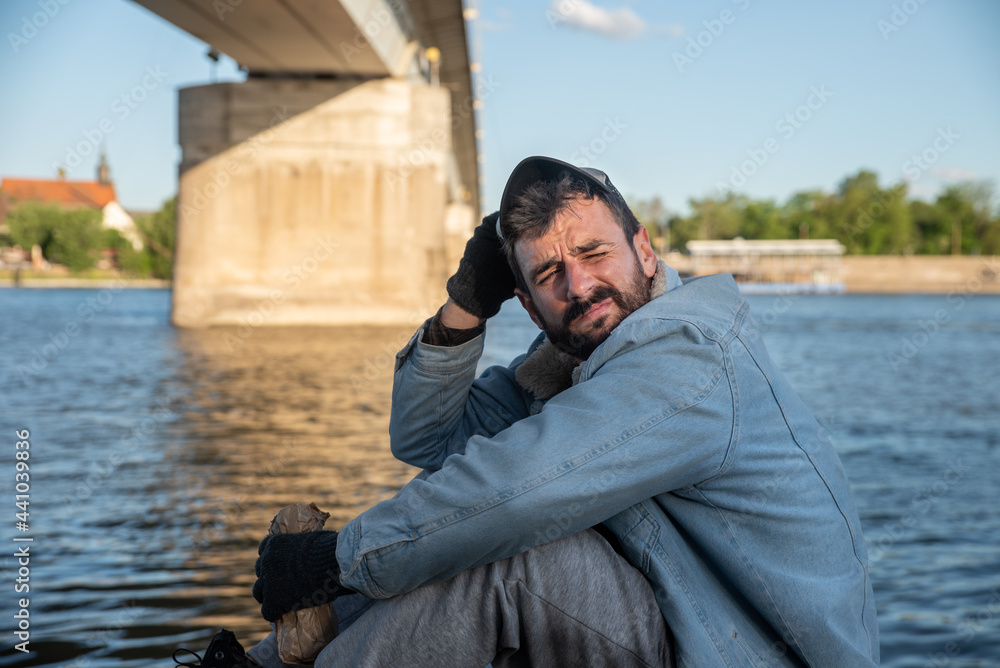 Young depressed alcoholic homeless man sitting under the bridge ...