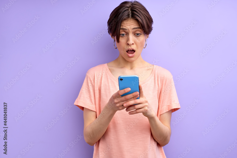 Lovely Woman Surprised By Getting Message, Get News, In Shock, Emotionally Reacts On News in Smartphone, Standing With Opened Mouth Lovely Woman Surprised By Getting Message, Get News, In Shock, Emotionally Reacts On News in Smartphone, Standing With Opened Mouth