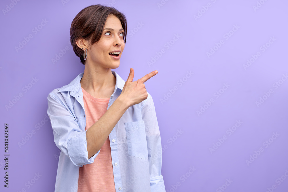 woman indicates finger at side on empty space advising product for buyers, copy space. isolated purple background, portrait, side view woman indicates finger at side on empty space advising product for buyers, copy space. isolated purple background, portrait, side view