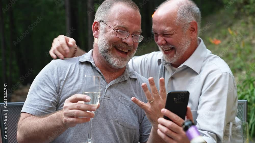 Two gay men have video chat on phone with friends showing their engagement ring for their marriage. Two gay men have video chat on phone with friends showing their engagement ring for their marriage.