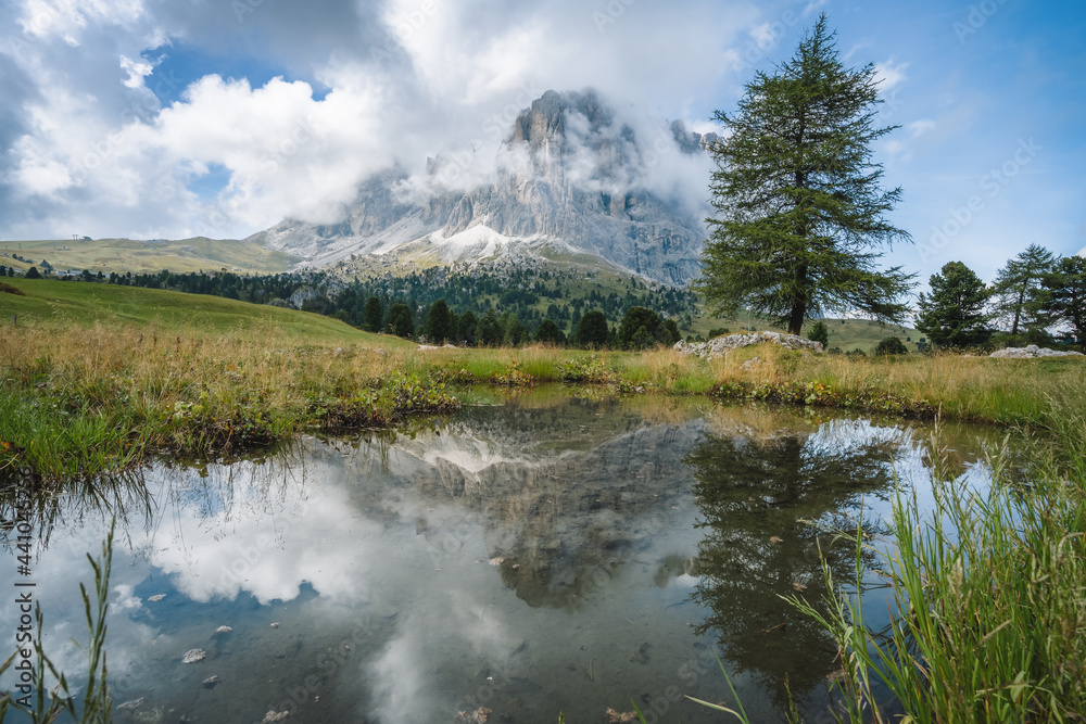 Woman hiking in Val Gardena. Pond and reflection of Sassolungo Langkofel mountain. Dolomites, Italy