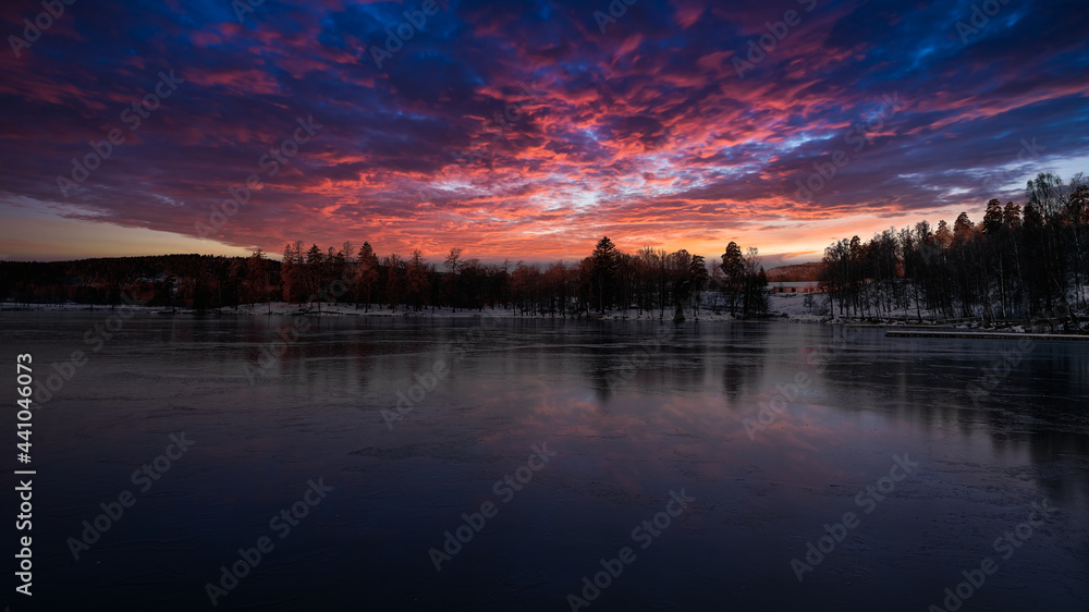 Ice cold reflections. The lake is frozen, the sky is on fire and reflecting in the ice. Shot in Norway, Oslo marka. 