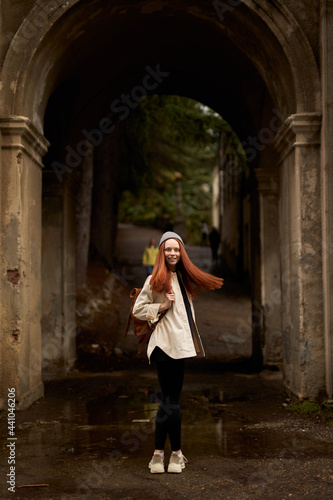 Young woman tourist enjoying beautiful abandoned place or site, walking alone. Redhead caucasian lady in coat and hat outdoors, with backpack. vacation, holidays, tourism, travel concept © alfa27