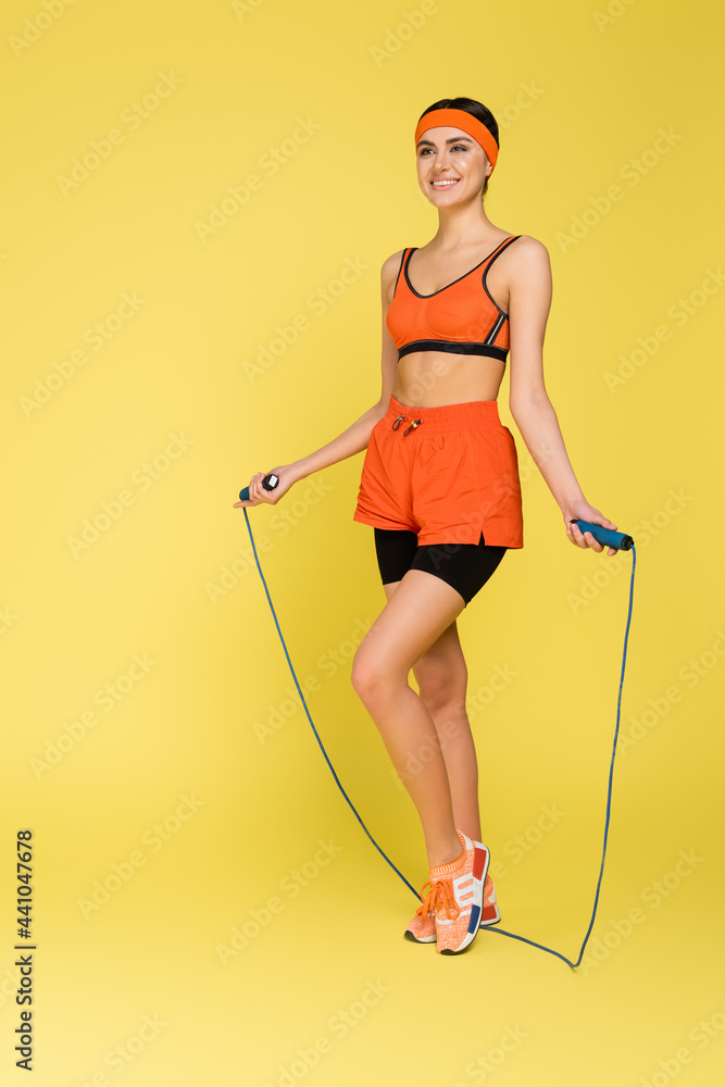 Φωτογραφία full length view of happy woman in orange sportswear with jump rope on yellow background