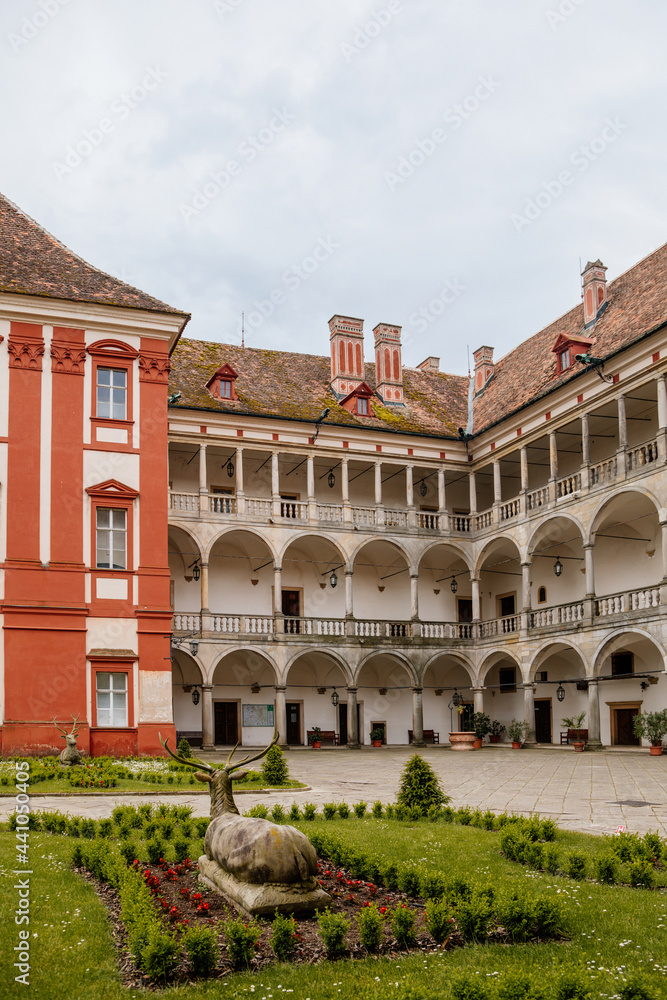 Opocno castle, renaissance chateau, courtyard with arcades and red facade, green lawn with statue and flowers in foreground, sunny summer day, aristocratic residence, Czech Republic