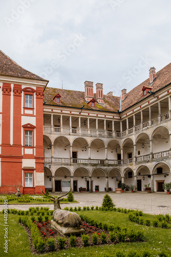 Opocno castle, renaissance chateau, courtyard with arcades and red facade, green lawn with statue and flowers in foreground, sunny summer day, aristocratic residence, Czech Republic