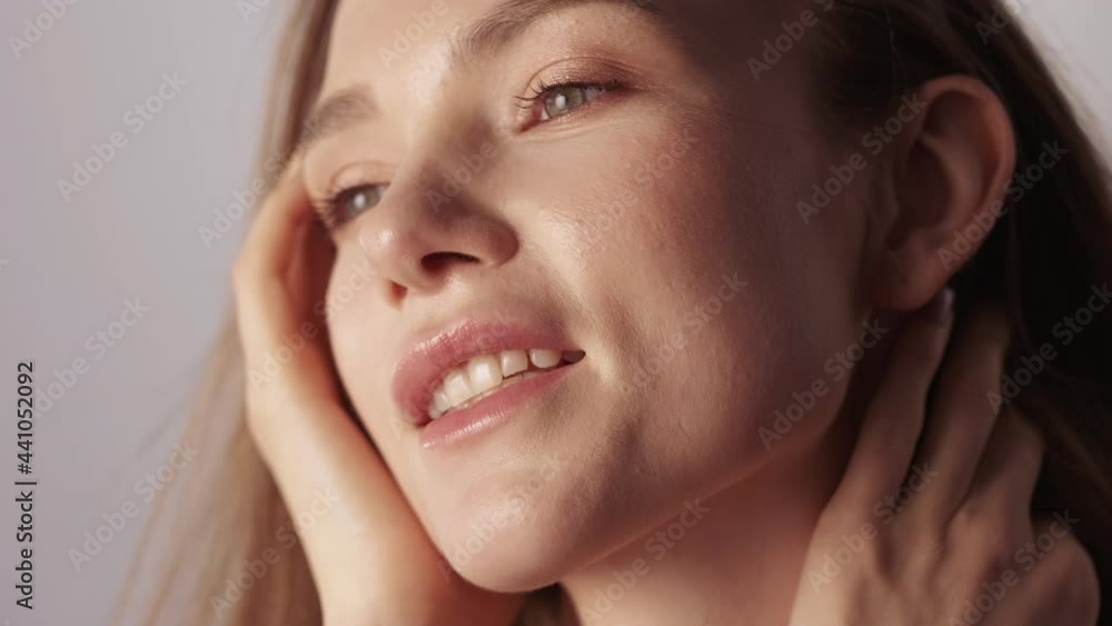 Healthy beauty. Natural skincare. Facial treatment. Freshness wellbeing. Smiling brunette woman with nude makeup flying hair enjoying touching radiant face skin isolated on beige. Healthy beauty. Natural skincare. Facial treatment. Freshness wellbeing. Smiling brunette woman with nude makeup flying hair enjoying touching radiant face skin isolated on beige.