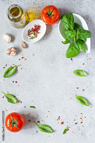 Fresh vegetables and herbs with spices on a gray background. Food background. Flatlay of ripe tomato, fresh basil leaves, garlic and spices, healthy food concept, copy space.