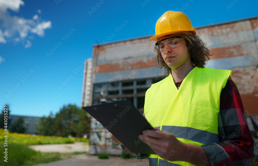 Male contractor in hard hat inspects abandoned buildings. - obrazy, fototapety, plakaty 