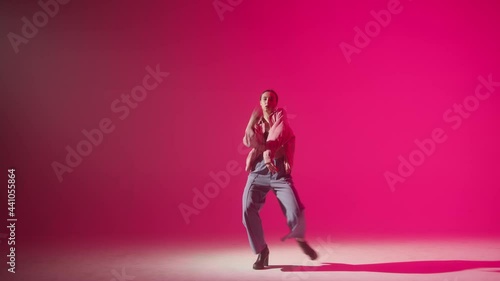 Young woman wearing high heels dancing contemporary on pink neon background in studio. Shooting of modern slow dance choreography. Motion of female dancer showing dance movings.  photo