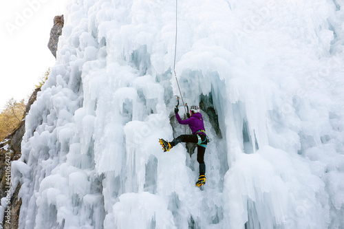 Alpinist woman with ice climbing equipment, axe and climbing ropes, climbing at a frozen waterfall, view from below
