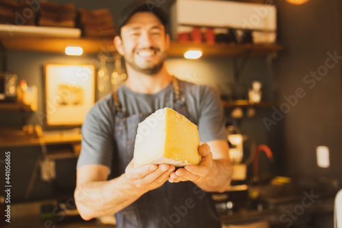 Barista offering big nice piece of cheese with both hands in Brazilian organic artisanal bakery. Small business concept. Shop shelf out of focus on the background. photo