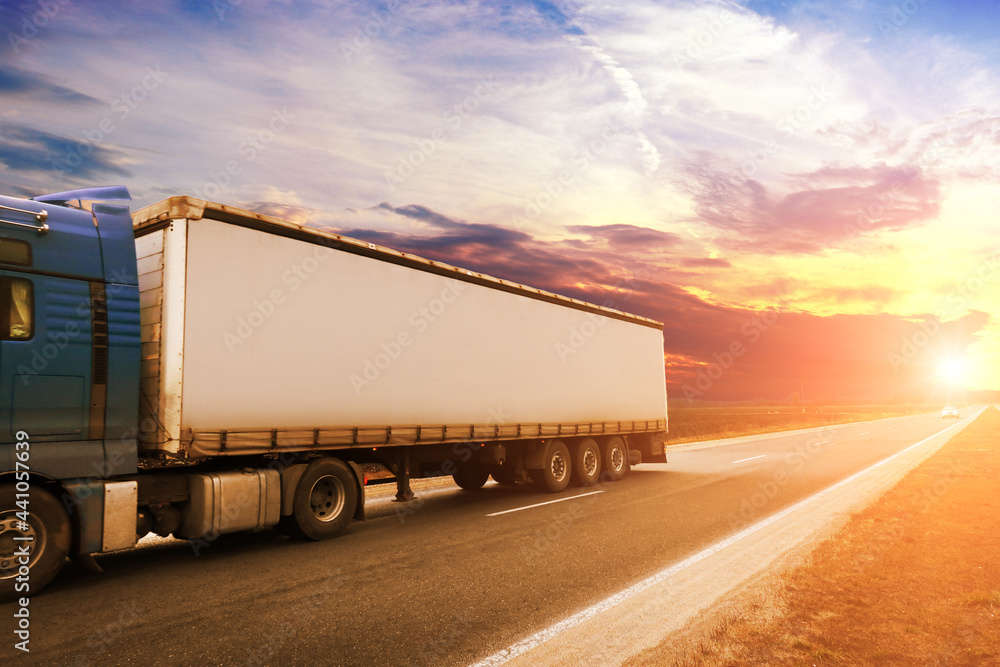 A big truck with a trailer on a road with other cars against a sky with a sunset