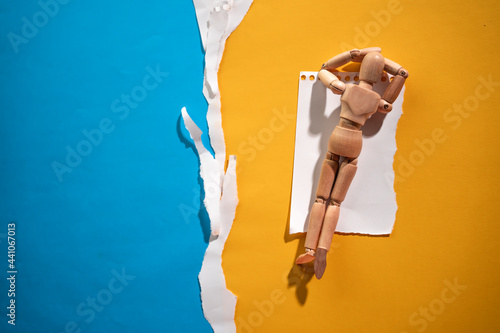 wooden mannequin sunbathing on the beach - torn paper backdrop photo