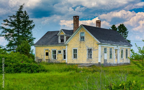 Old and abandoned house in rural Maine with dramatic clouds overhead on summer's day.