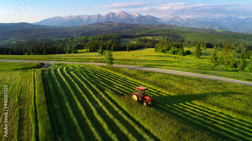 Tractor mowing the grass with beautiful high mountains in the background  aerial view. Haymaking in the mountain village. Tractor during harvest. Ecological agriculture. 