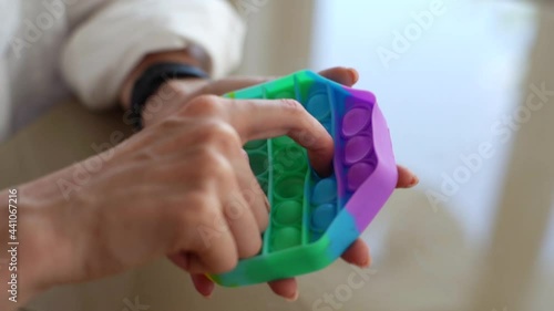 Wallpaper Mural Close-up hands of unrecognizable young woman playing with multicolored pop-it fidget toy sitting at table. Closeup top view of female pushing colorful iridescent soft silicone bubbles sitting at desk. Torontodigital.ca