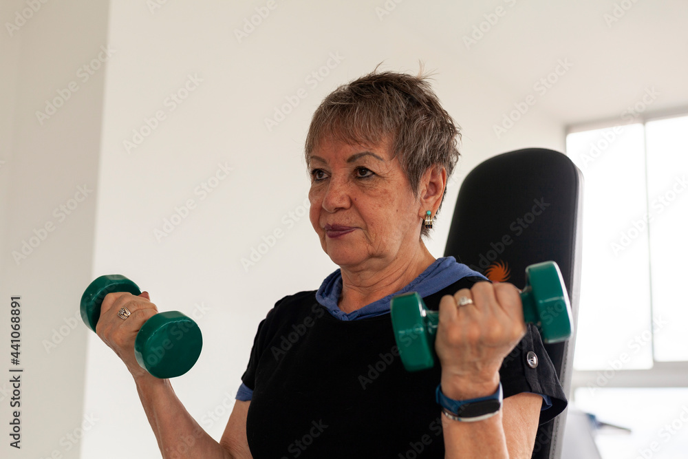 72-year-old grandmother works out in a gym doing weight routines and practicing exercise on a stationary bike. 72-year-old grandmother works out in a gym doing weight routines and practicing exercise on a stationary bike.