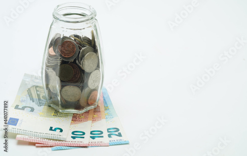 Thai baht and euro coins are placed together in a glass bottle with euro banknotes placed under the bottle. isolated white background concept of spending money and saving money has copy space.