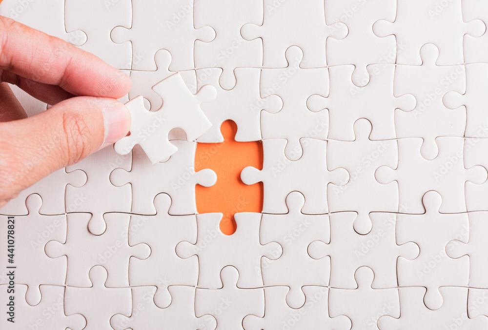 Top view flat lay of hand-holding last piece white paper jigsaw puzzle game last pieces put to place for solve problem complete mission, studio shot on an orange background, quiz calculation concept Top view flat lay of hand-holding last piece white paper jigsaw puzzle game last pieces put to place for solve problem complete mission, studio shot on an orange background, quiz calculation concept