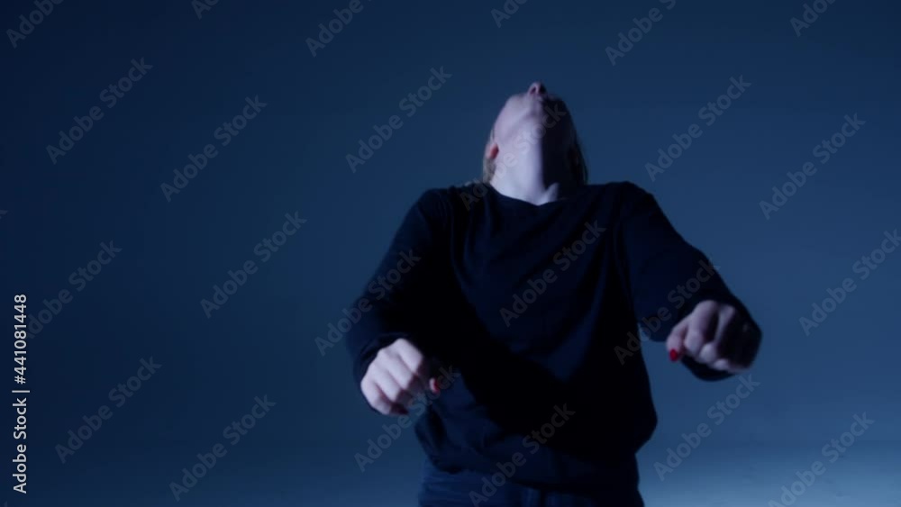 Close-up of teenager with long hair wearing black clothes dancing contemporary on dark neon background in studio. Shooting of modern slow choreography, dancer expressing feelings for music video. Close-up of teenager with long hair wearing black clothes dancing contemporary on dark neon background in studio. Shooting of modern slow choreography, dancer expressing feelings for music video.