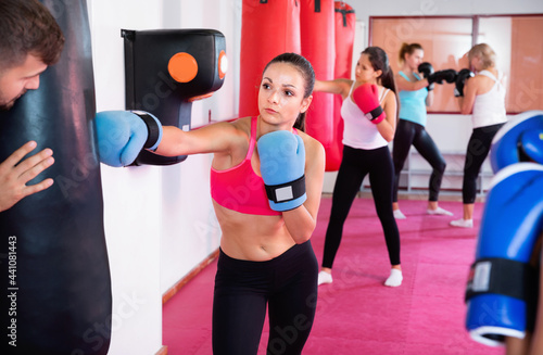 Sporty efficient glad girl is boxing near punching bag in gym.