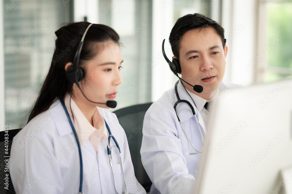 Asia medical service team health advice online. Smiling face stood wearing the headphones with a microphone and stethoscope in clinics.Concept of remote medicine, health care call center online. Asia medical service team health advice online. Smiling face stood wearing the headphones with a microphone and stethoscope in clinics.Concept of remote medicine, health care call center online.