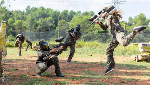 Dynamic paintball battle. Portrait female player jumping and aiming marker on player of opposing team.