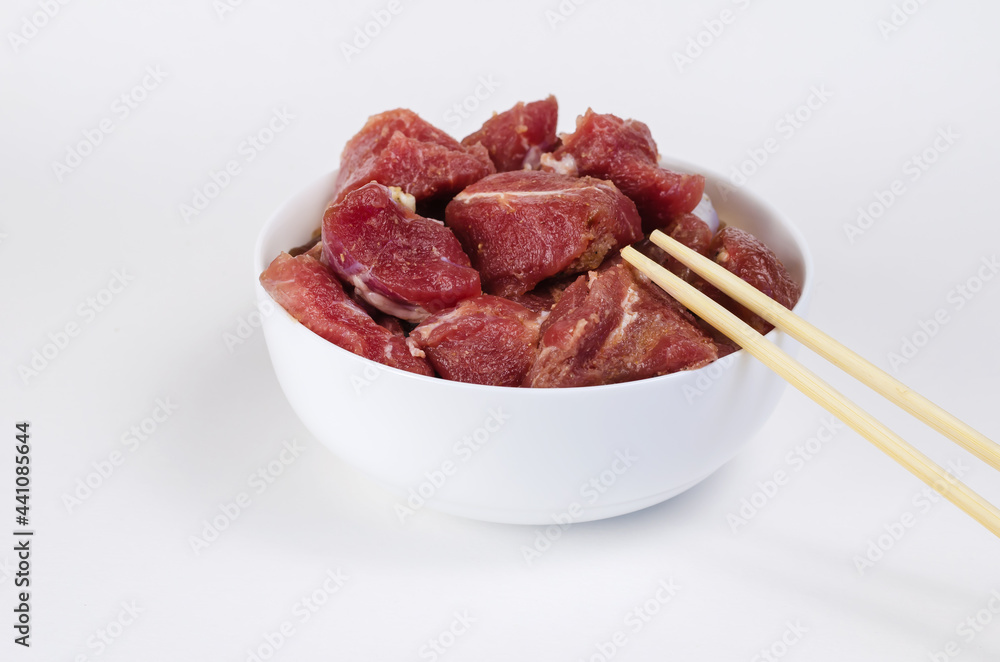 Ceramic bowl with raw marinated meat and bamboo sticks on a whit Ceramic bowl with raw marinated meat and bamboo sticks on a whit