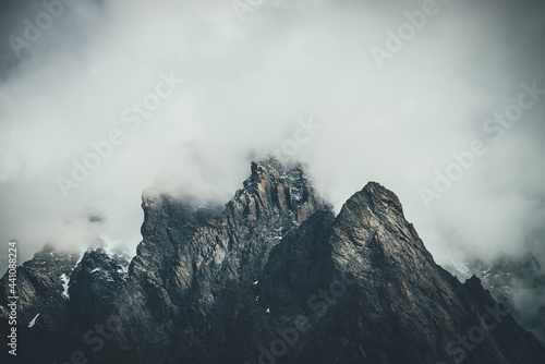 Photography Dark atmospheric surreal landscape with dark rocky mountain top in low clouds in gray cloudy sky