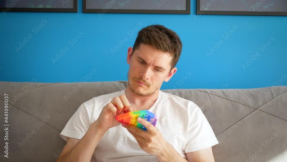 A man sits on the couch picks up a pop it and tries to figure out how to use it. Anti stress instruction A man sits on the couch picks up a pop it and tries to figure out how to use it. Anti stress instruction