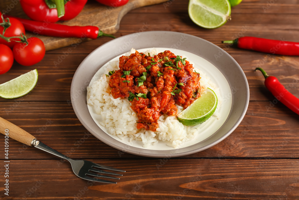 Plate with tasty chili con carne, rice, lime and vegetables on wooden background Plate with tasty chili con carne, rice, lime and vegetables on wooden background