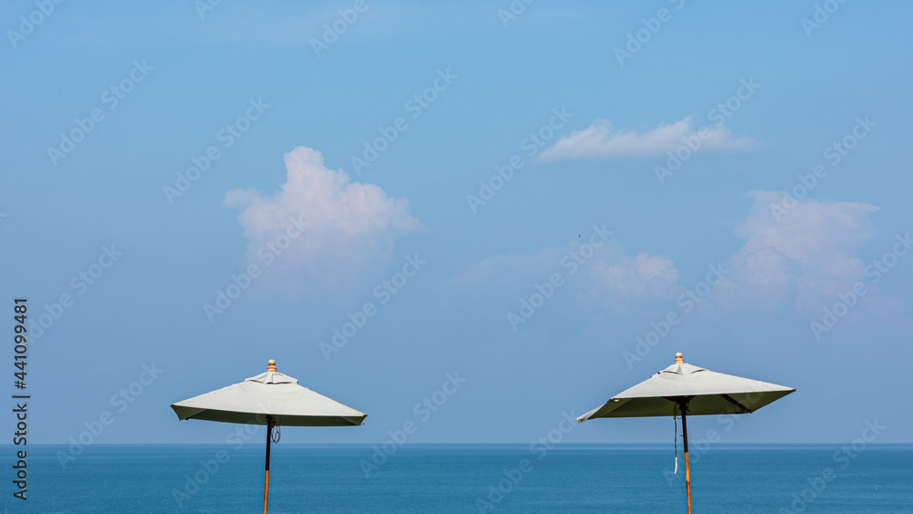 Beach umbrella as foreground at a peaceful and clean tropical sandy beach under blue cloudy sky on sunny day