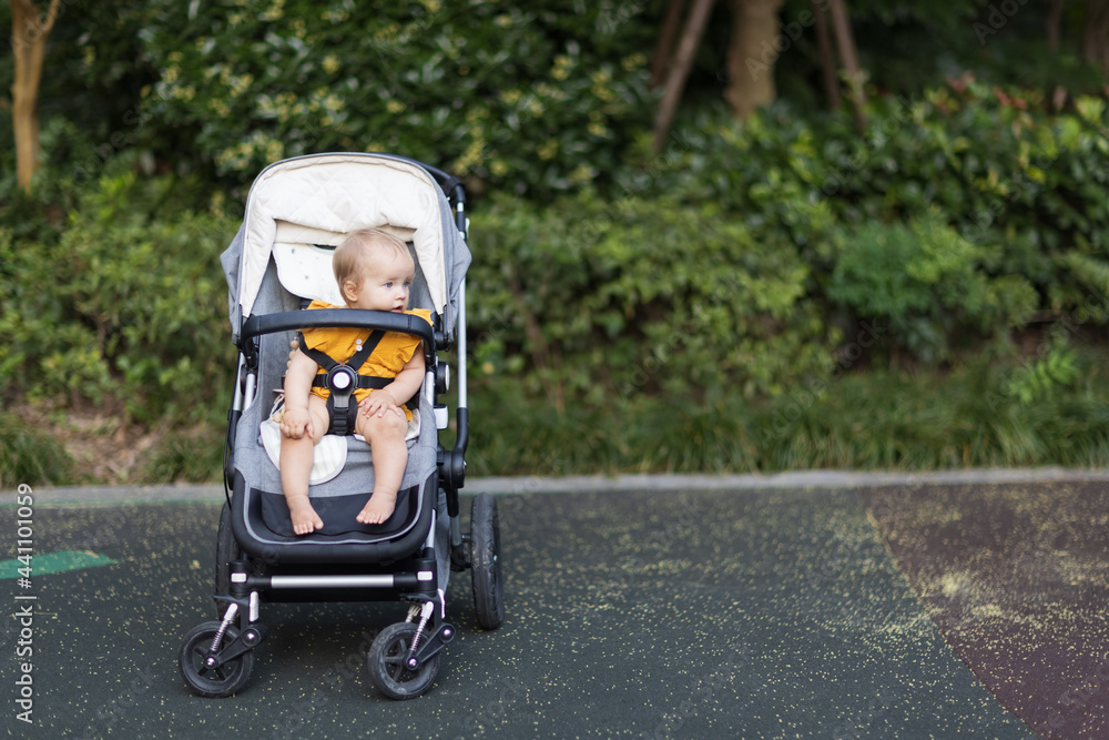 Sweet caucasian baby girl ten months old sitting in stroller outdoors. Little child in pram. Infant kid sits in pushchair. Summer walks with kids. Family leisure with little child. Sweet caucasian baby girl ten months old sitting in stroller outdoors. Little child in pram. Infant kid sits in pushchair. Summer walks with kids. Family leisure with little child.