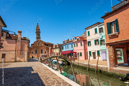 Burano island, multi colored houses, small canal with moored boats and the Parish church of San Martino Vescovo (Saint Martin Bishop) with the leaning bell tower (XVI century), Venice, Veneto, Italy. © Alberto Masnovo