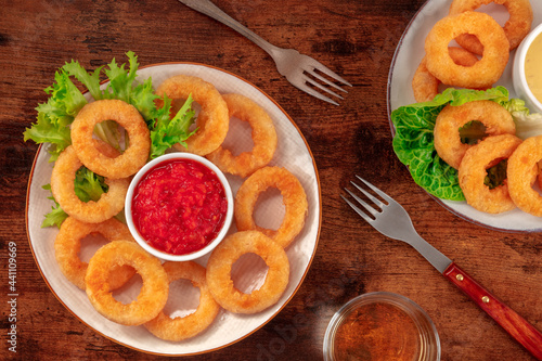 Calamari rings. Deep fried squid rings with ketchup and green salad, overhead flat lay shot on a dark rustic wooden background