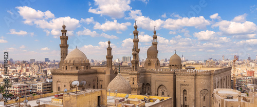 Aerial day shot of minarets and domes of Sultan Hasan mosque and Al Rifai Mosque mediating shabby buildings with satellite dishes in cloudy day, Old Cairo, Egypt