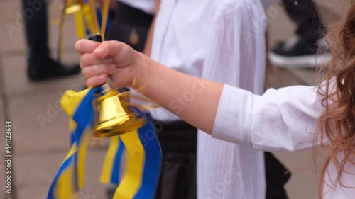 Golden colored school bell decorated of blue and yellow ribbon dinging in a hand of little schoolgirl at sunny day. Back to school concept.
