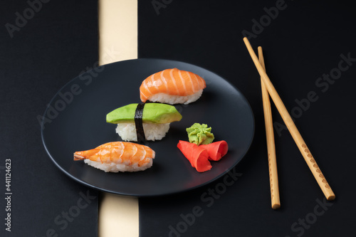 Japanese cuisine - set of nigiri sushi with salmon, avocado ans schrimp on a black plate with chopsticks.