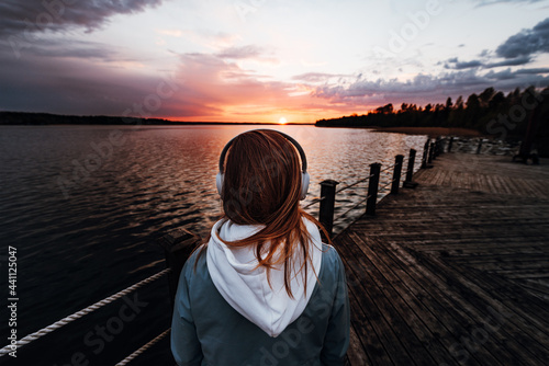The girl listens to music with headphones stands on the pier near the lake and looks at the sunset,ASMR concept photo