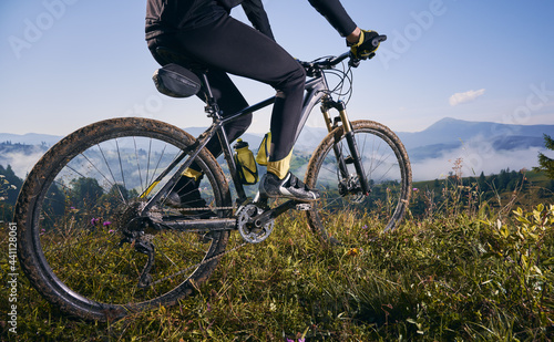Close up, low angle view on a bike with cyclist. Man's legs riding his bicycle on grass in summer in the mountains against blue sky. Concept of extreme cycling