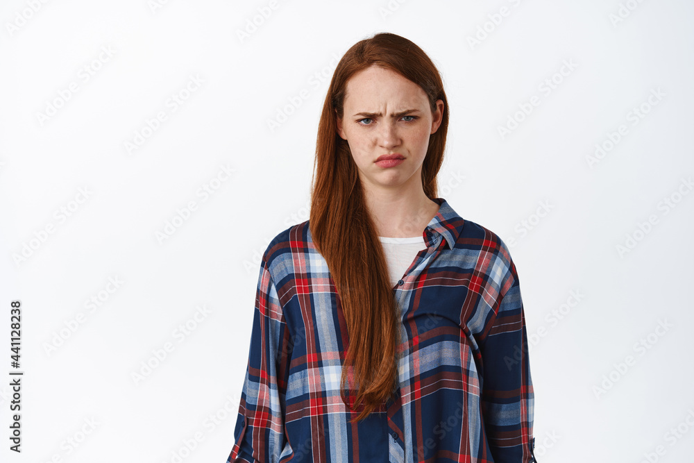 Portrait of grumpy and angry redhead woman, look hurt at unfair thing, frowning and sulking, standing upset and offended against white background Portrait of grumpy and angry redhead woman, look hurt at unfair thing, frowning and sulking, standing upset and offended against white background