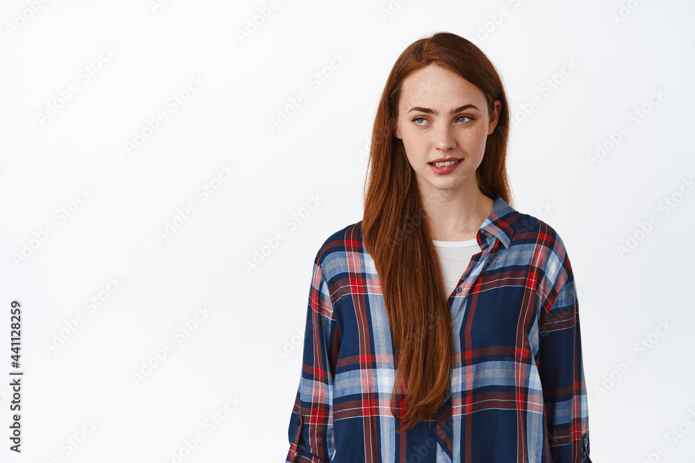 Sensual young redhead woman biting lip, looking aside at logo with thoughtful coquettish face expression, standing against white background Sensual young redhead woman biting lip, looking aside at logo with thoughtful coquettish face expression, standing against white background