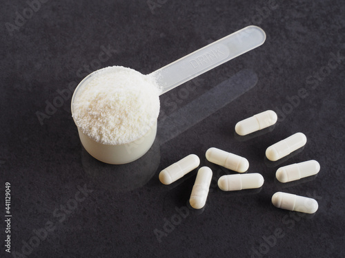 Protein powder, capsules, chondroitin, glucosamine in a plastic spoon for making a high-calorie drink on a dark background, closeup, flat layout. Healthy sports nutrition for fitness photo