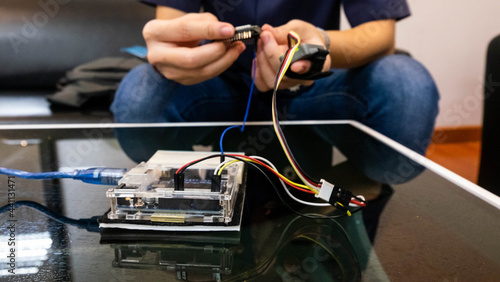 Close up student hand connecting wires on breadboard with Arduino board while coding on laptop, DIY electronics project, microcontroller programming, STEM, hands on learning and hardware prototyping.