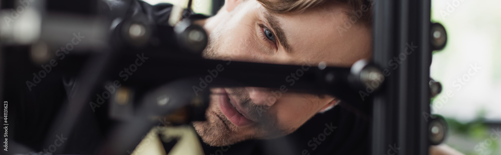 Fototapeta premium close up view of concentrated young designer looking at 3D printer in modern office, banner