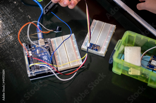 Close-up of a person assembling an Arduino Uno circuit using a breadboard and jumper wires. One hand carefully holds a module, while the other hand balances the components during setup.